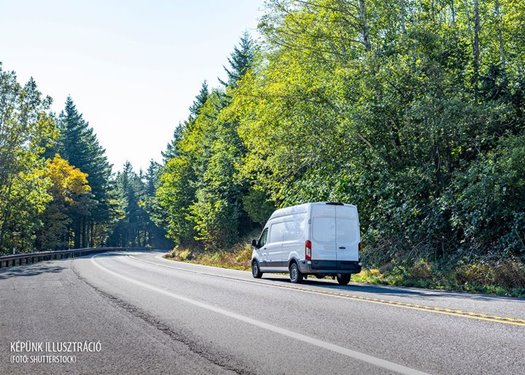 Compact small size white mini van with cargo compartment for local deliveries and small business needs for customers commercial cargo delivery driving on the turning road with forest on the sides