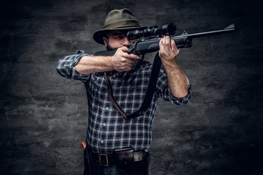 studio portrait bearded hunter male wearing plaid fleece shirt holds rifle