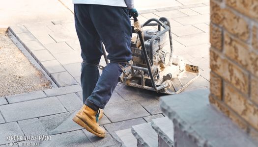 Landscaping worker contractor using plate compactor to apply polymeric joint sands on interlock pavers. Home garden and landscape renovation project background. 