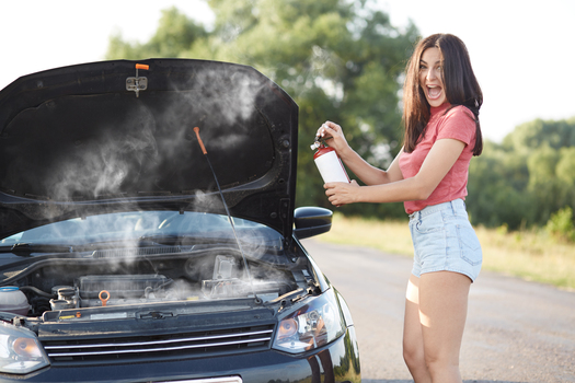 Depressed brunette female driver stands near brocken car with opened hood, tries to solve technical problem by herself while waits for auto technician, opens mouth widely, exclaims in great despair