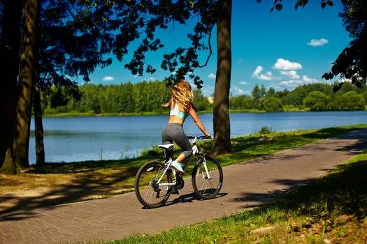Back of sexy hot sport blond woman girl model  riding on bicycle in the green summer park near lake with flying elevated hair in air