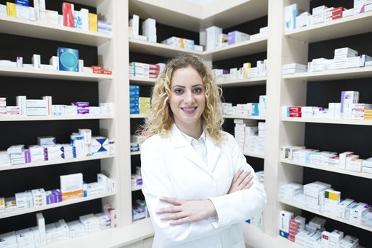 Portrait of female pharmacist in drug store standing in front of shelves with medications.