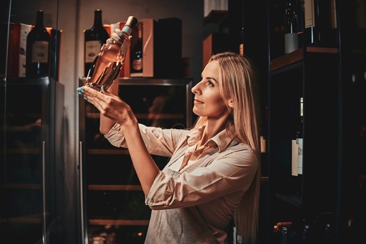 Beautiful focused woman is choosing right wine for customers at dark wine cellar.