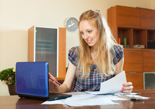 Positive long-haired woman working with financial documents and laptop at home interior