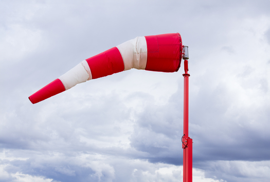 Striped red and white weather vane flies in wind in the background with dark blue cloudy sky before storm.