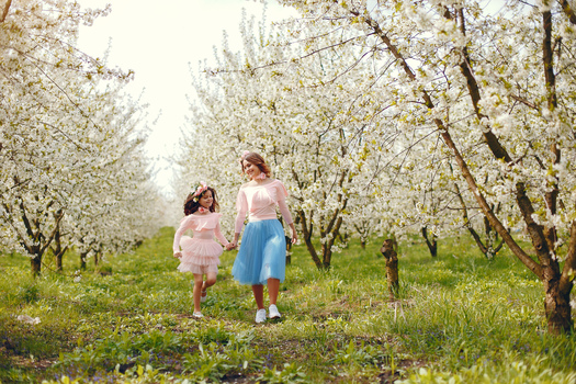 Pretty mother with daughter. Family in a spring park. Woman in a pink dress. Child with a flowers