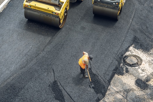 Workers lay a new asphalt coating using hot bitumen. Work of heavy machinery and paver. The view from the top