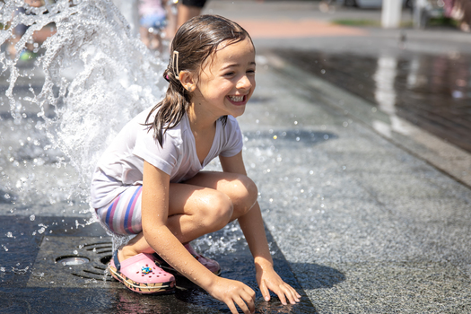 A little wet girl is cooling off in a fountain on a hot summer day.